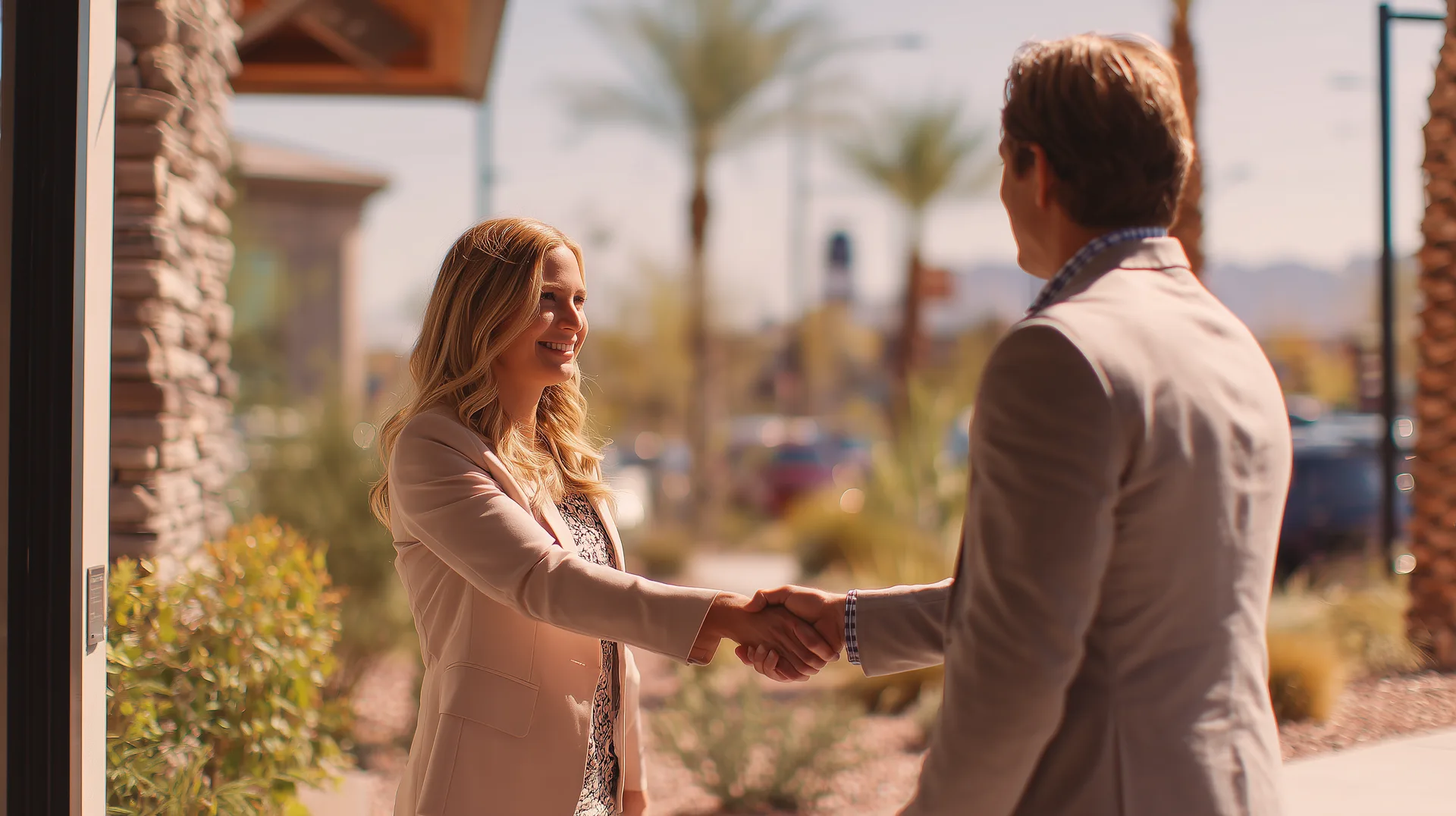 Two people shaking hands outside a builder sales office with palm trees in background